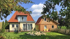 A two-story house with a red roof, a patio with outdoor furniture, and a well-maintained garden. - Ferienhaus, Fedderwardersiel (Butjadingen)