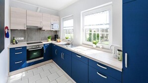 A modern kitchen with blue cabinets, a white countertop, and a window providing a view of the outdoors. - Ferienhaus, Fedderwardersiel (Butjadingen)