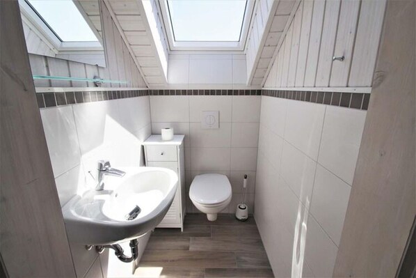 Une petite salle de bain dotée d’un puits de lumière, d’un lavabo, de toilettes et d’un bidet.