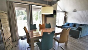 A modern dining area with a wooden table and chairs, a sofa, and a TV in the background. - Exklusives Skandinavisches Ferienhaus (Mirow)