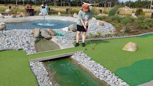 A miniature golf course with a water hazard, green artificial turf, and a rocky border. - Charming Retreat in Nordjylland - By Traum Ferienwohnungen (Blokhus)