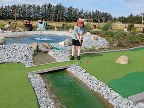 A miniature golf course with a water hazard, green artificial turf, and a rocky border.
