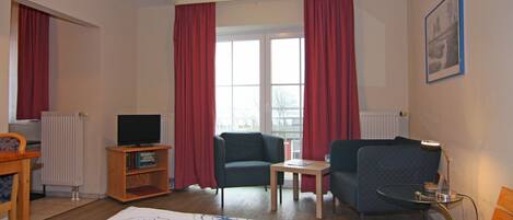Habitación de hotel con cama, dos sillones, una mesita, televisor y ventana con cortinas.