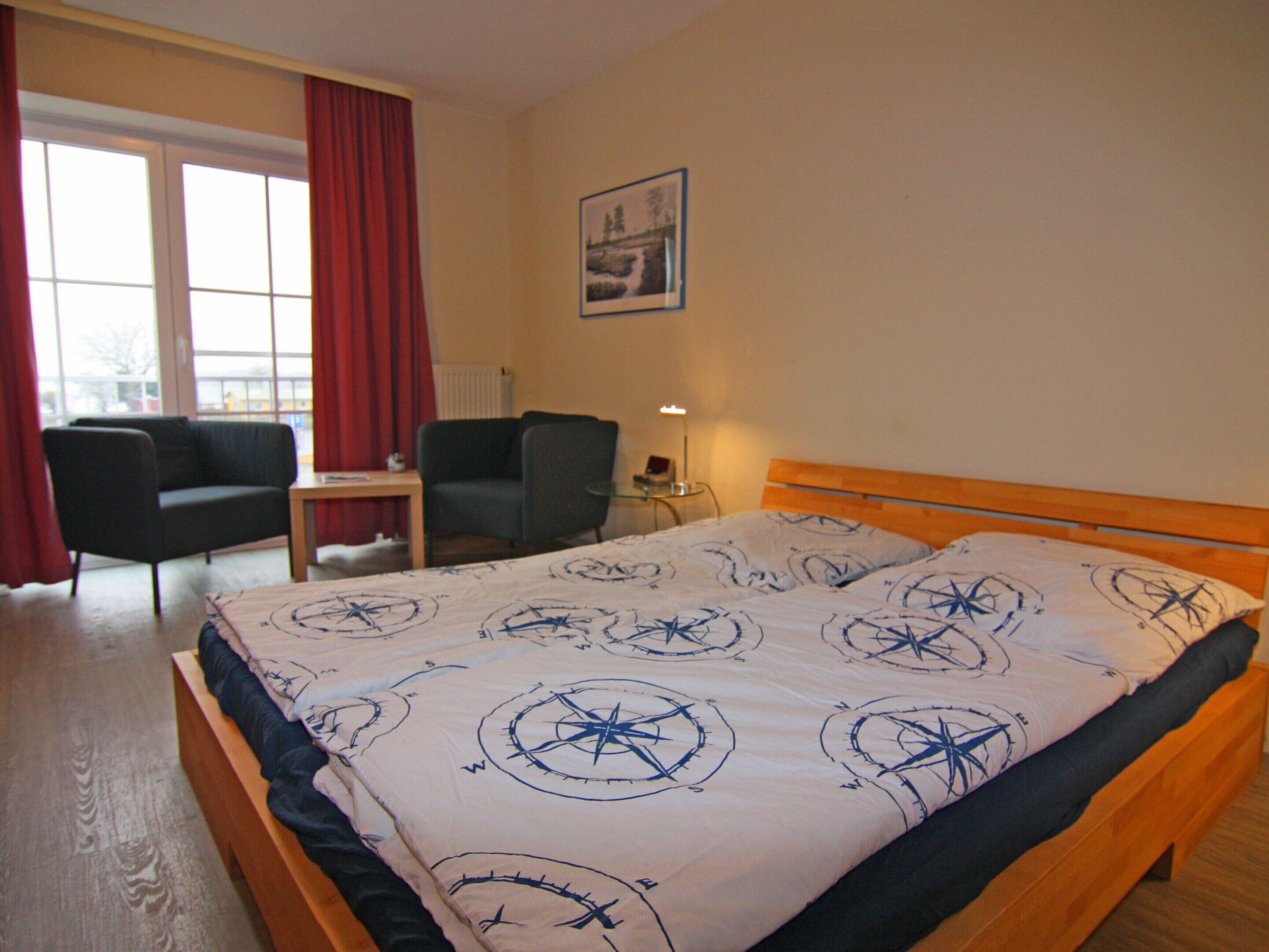 A hotel room with a bed, a chair, a small table, and a window with curtains.