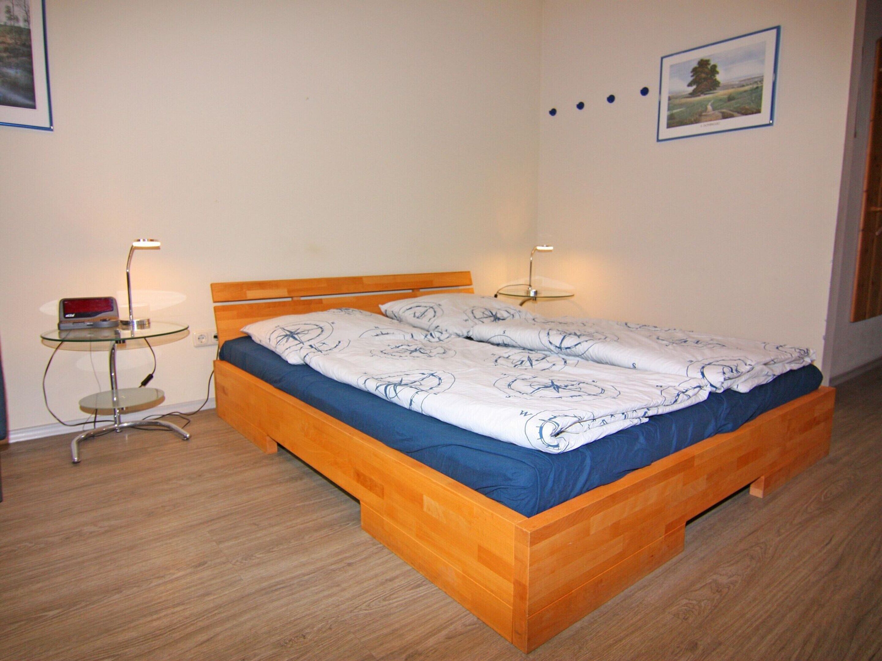 A single bed with a wooden frame and a blue and white patterned bedspread. There are two bedside tables with lamps, one on each side of the bed. The room has light-colored walls and a wooden floor.