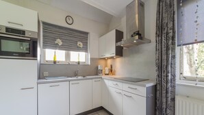 A compact kitchen with white cabinets, a built-in microwave, a coffee maker, and a window with a view of trees. - Holiday Home in Zeeland With Spacious Garden (Wemeldinge)