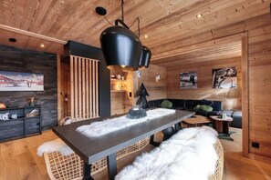 A modern interior with a wooden ceiling, a central table with a black lamp, a sofa, and a wall-mounted shelf with decorative items. - Cosy apartment with mountain view, near village (Megève)