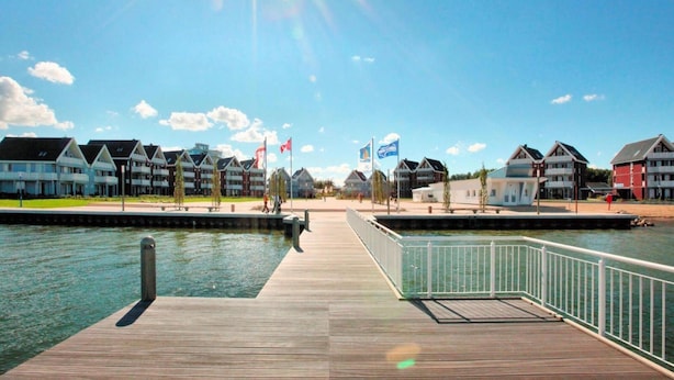 Un hotel frente al agua con un muelle de madera, cielo despejado y varias banderas.