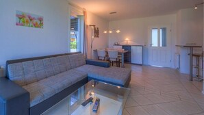 A modern living room with a sectional sofa, a glass coffee table, and a dining area with a small kitchen in the background. - Ferienwohnung im Ferienpark Mueritz (Rechlin)