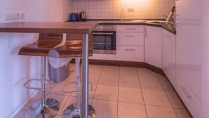 A modern kitchen with white cabinets, a stainless steel stove, and a bar stool area. - Ferienwohnung im Ferienpark Mueritz (Rechlin)