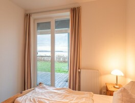 A bedroom with a bed, a nightstand with a lamp, and a view of a grassy area through a sliding glass door.
