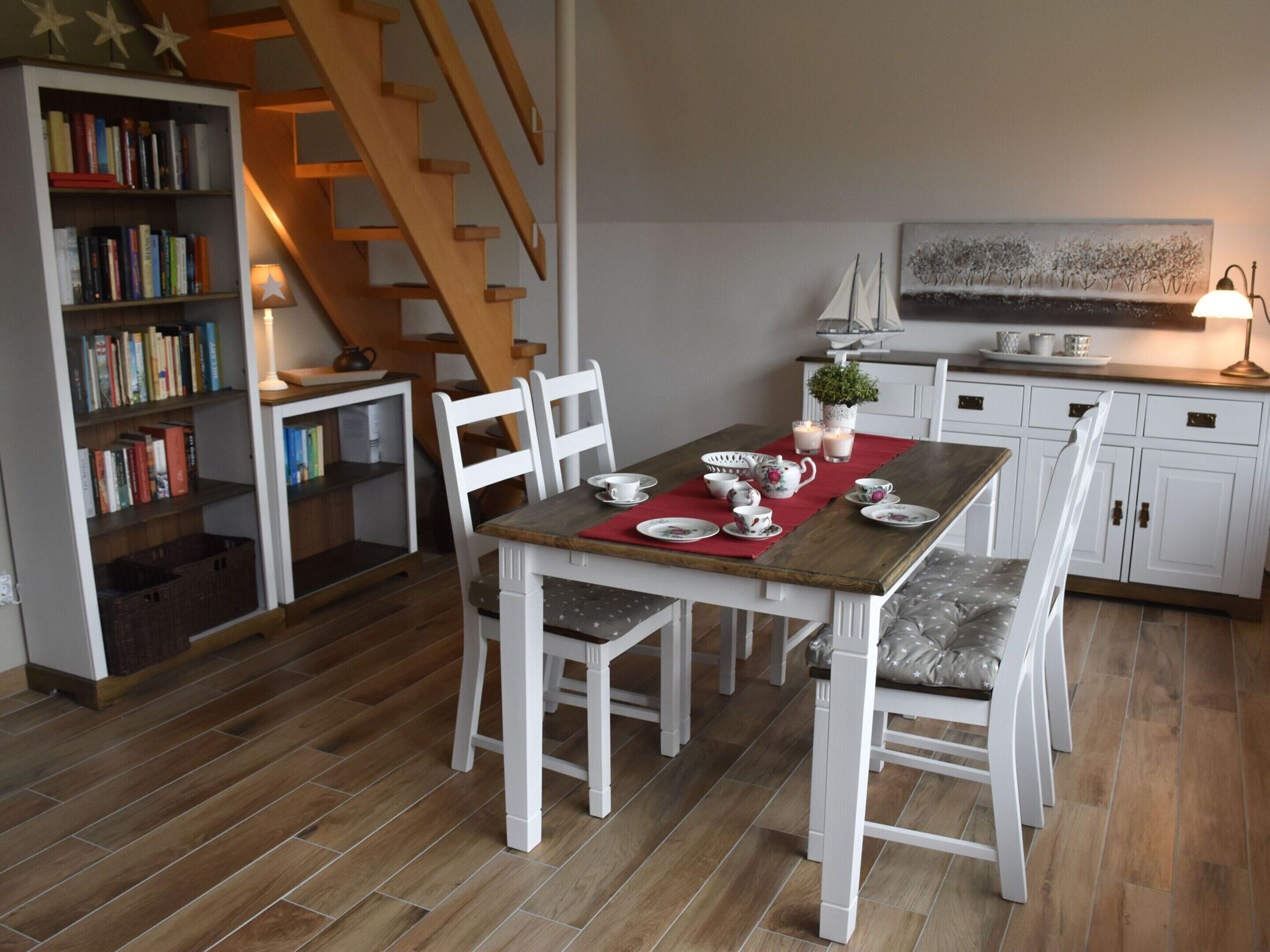 A dining area with a wooden table, white chairs, and a bookshelf filled with books.