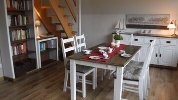 A dining area with a wooden table, white chairs, and a bookshelf filled with books.