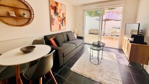 A modern living room with a sofa, a dining table, and chairs. There is a painting on the wall and a ceiling light. - T2 with terrace near Les Minimes (La Rochelle)