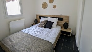 A bedroom with a bed, a window, a radiator, and wall decor. - T2 with terrace near Les Minimes (La Rochelle)