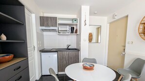 A compact kitchen with modern appliances, a dining table with chairs, and a small refrigerator. - T2 with terrace near Les Minimes (La Rochelle)