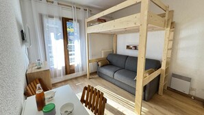 Een kamer met een stapelbed, een grijze bank, een eettafel met stoelen en een radiator.