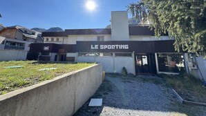A building with a sign reading "LE SPORTING" and a parking area in front.