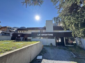 Rakennuksessa on kyltti, jossa lukee ”LE SPORTING”, ja sen edessä on parkkialue.