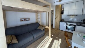 Een ruimtelijke leefruimte met een bank, kitchenette en houten balken.