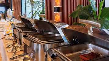 A buffet setup with various food containers, serving utensils, and a wooden panel wall with a vertical light fixture.