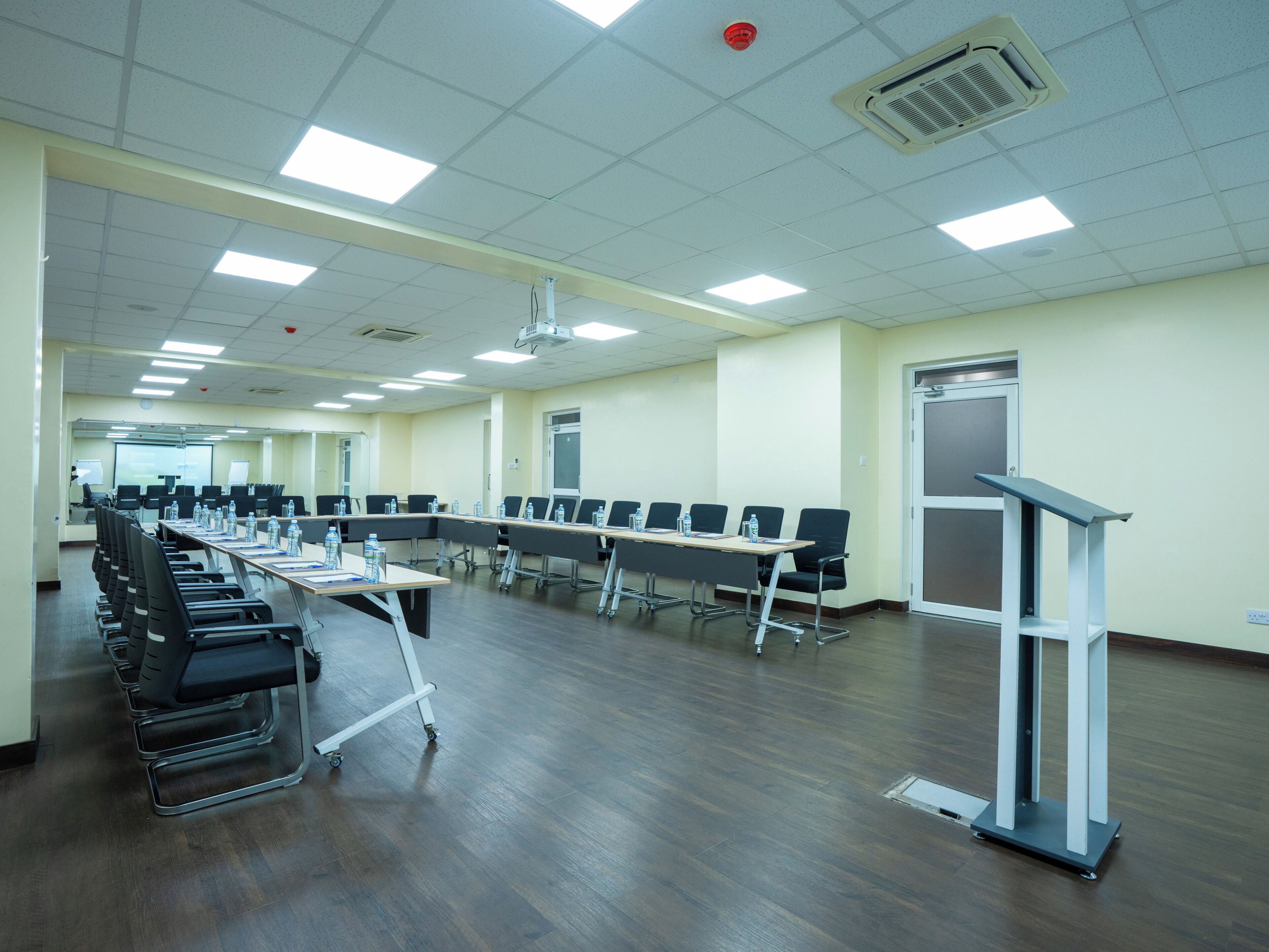 A conference room with a long table, chairs, a podium, and a projector screen.