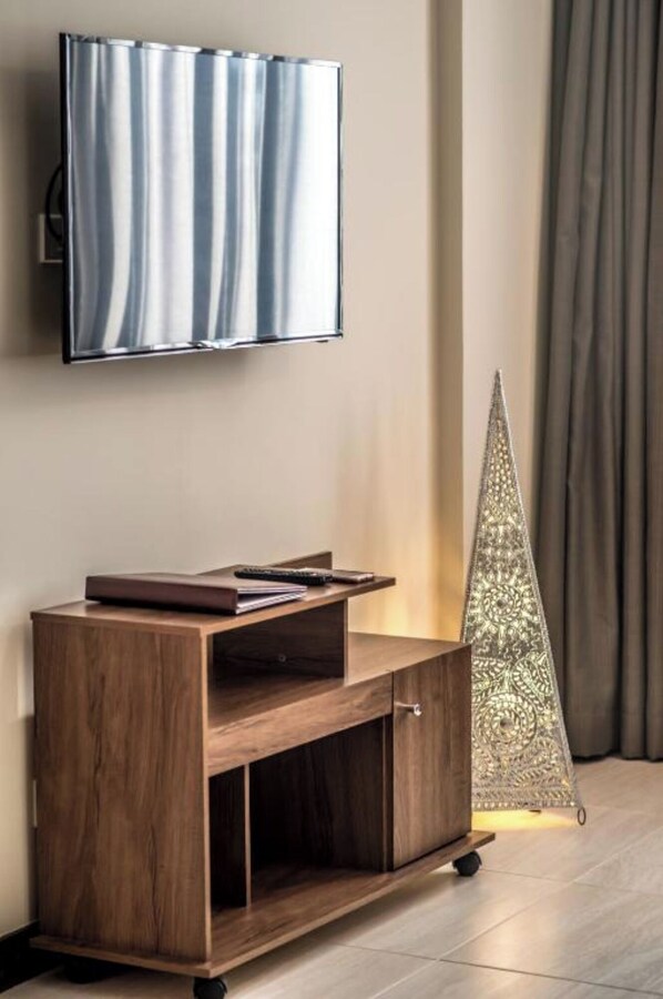 A wooden entertainment center with a flat-screen TV mounted above it, a decorative silver cone, and a curtain in the background. - Glam Hotel Nairobi, Near Westgate Mall, Westlands (Nairobi)