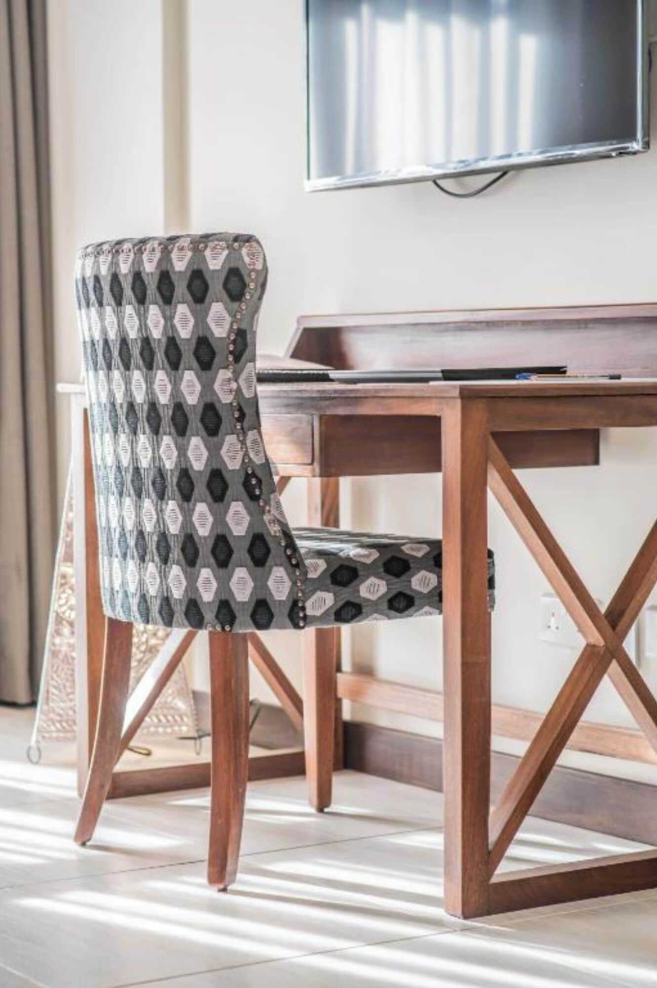 A wooden desk with a television mounted above it, a patterned chair, and a woven floor mat.