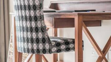 A wooden desk with a television mounted above it, a patterned chair, and a woven floor mat.