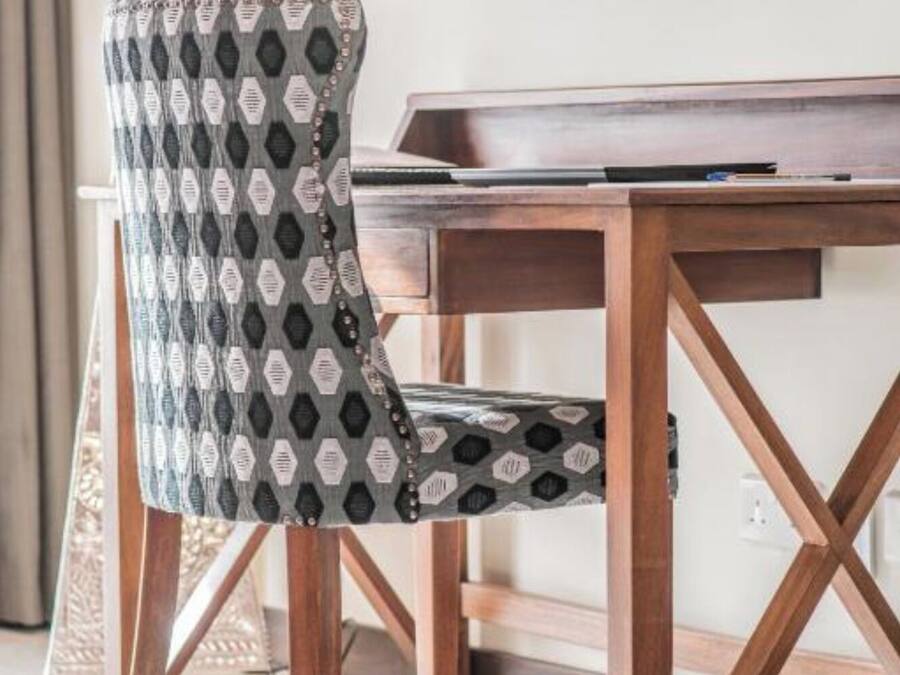 A wooden desk with a television mounted above it, a patterned chair, and a woven floor mat.