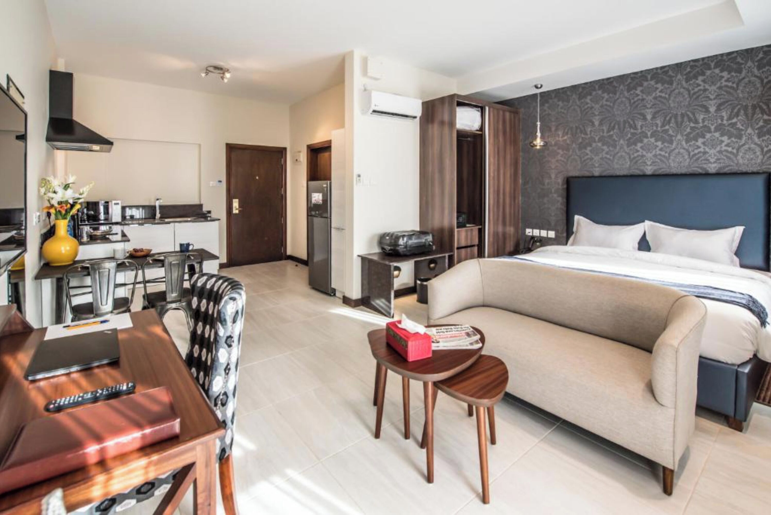 Une chambre d’hôtel moderne dotée d’un canapé-lit, d’un coin repas avec une table et des chaises, d’un coin cuisine et d’une grande fenêtre.