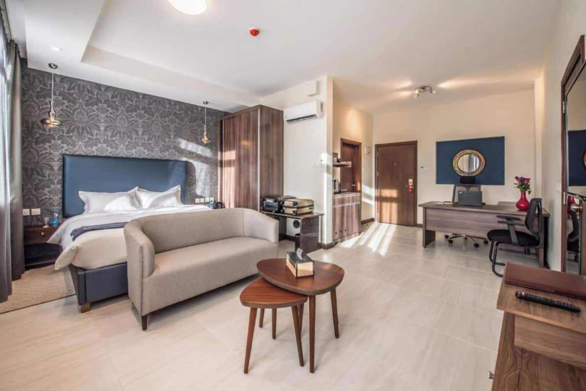 A modern hotel room with a large bed, a sofa, a desk, and a small table.