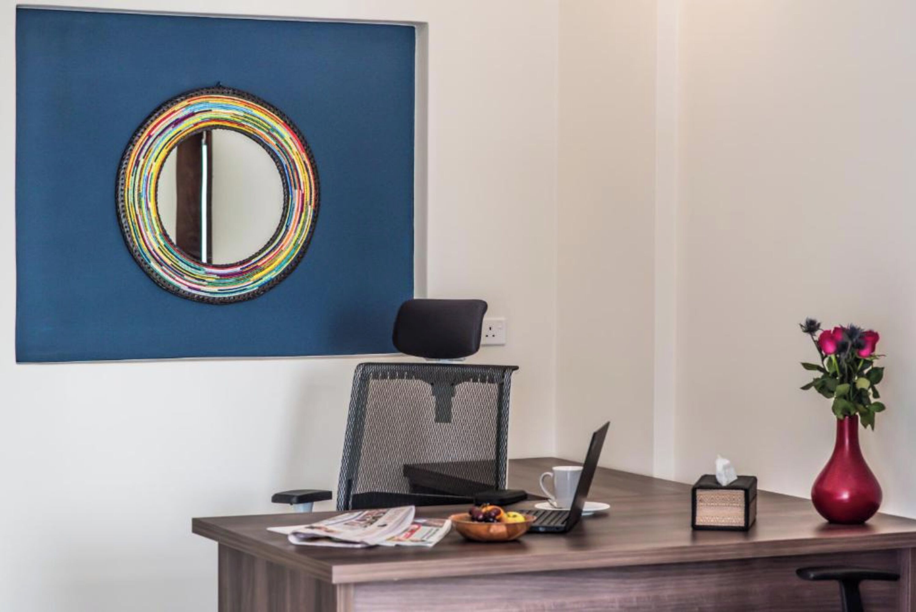 Un bureau moderne avec un ordinateur portable, un vase de fleurs, une boîte de mouchoirs et un saladier de fruits.