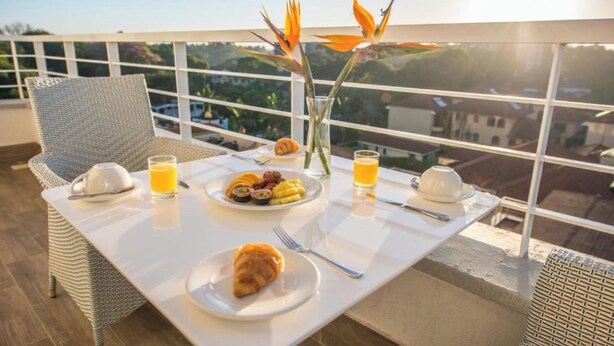 Een ontbijttafel met borden eten, een croissant en een glas sinaasappelsap op een balkon met uitzicht.