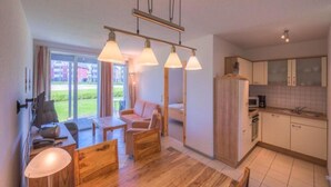 A modern living room with a wooden dining table, a sofa, and a kitchen area with cabinets and a microwave. - Tolles Appartment in der Seenplatte (Rechlin)