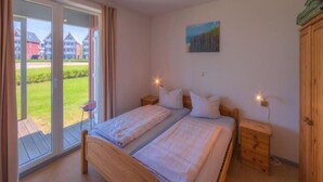 A bedroom with two beds, a sliding glass door to a balcony, a painting on the wall, and a wooden wardrobe. - Tolles Appartment in der Seenplatte (Rechlin)