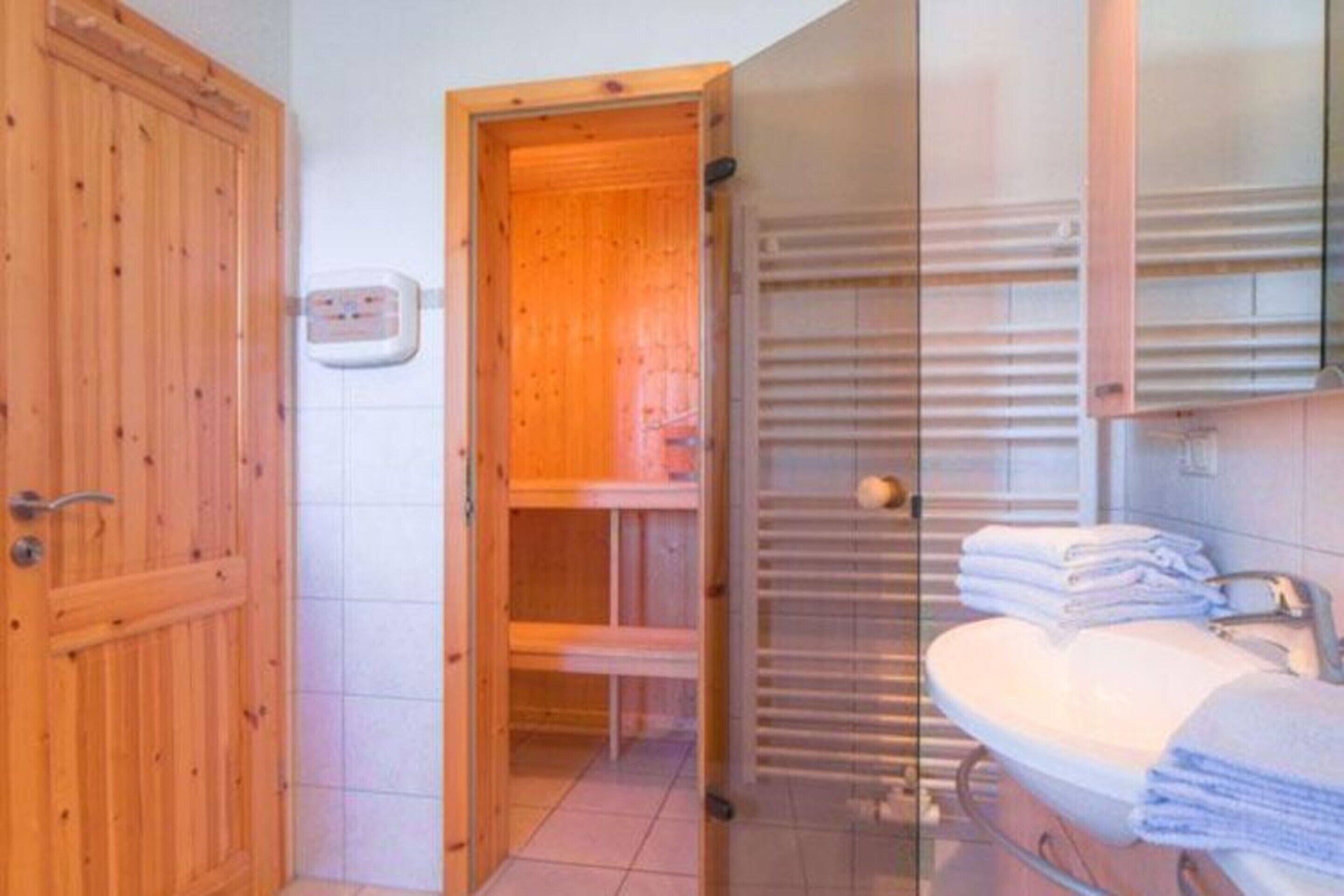 Ein Badezimmer mit Holztür, einer Bank, einem Handtuchhalter und einem Waschbecken mit gestapelten Handtüchern.