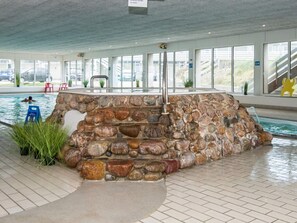 Relax by the tranquil pool surrounded by lush greenery and a natural rock feature.