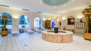 A spacious lobby with a central circular marble fountain, white lounge chairs, and large arched windows. - Appartement im Panoramic Hotel Bad Lauterberg (Bad Lauterberg)