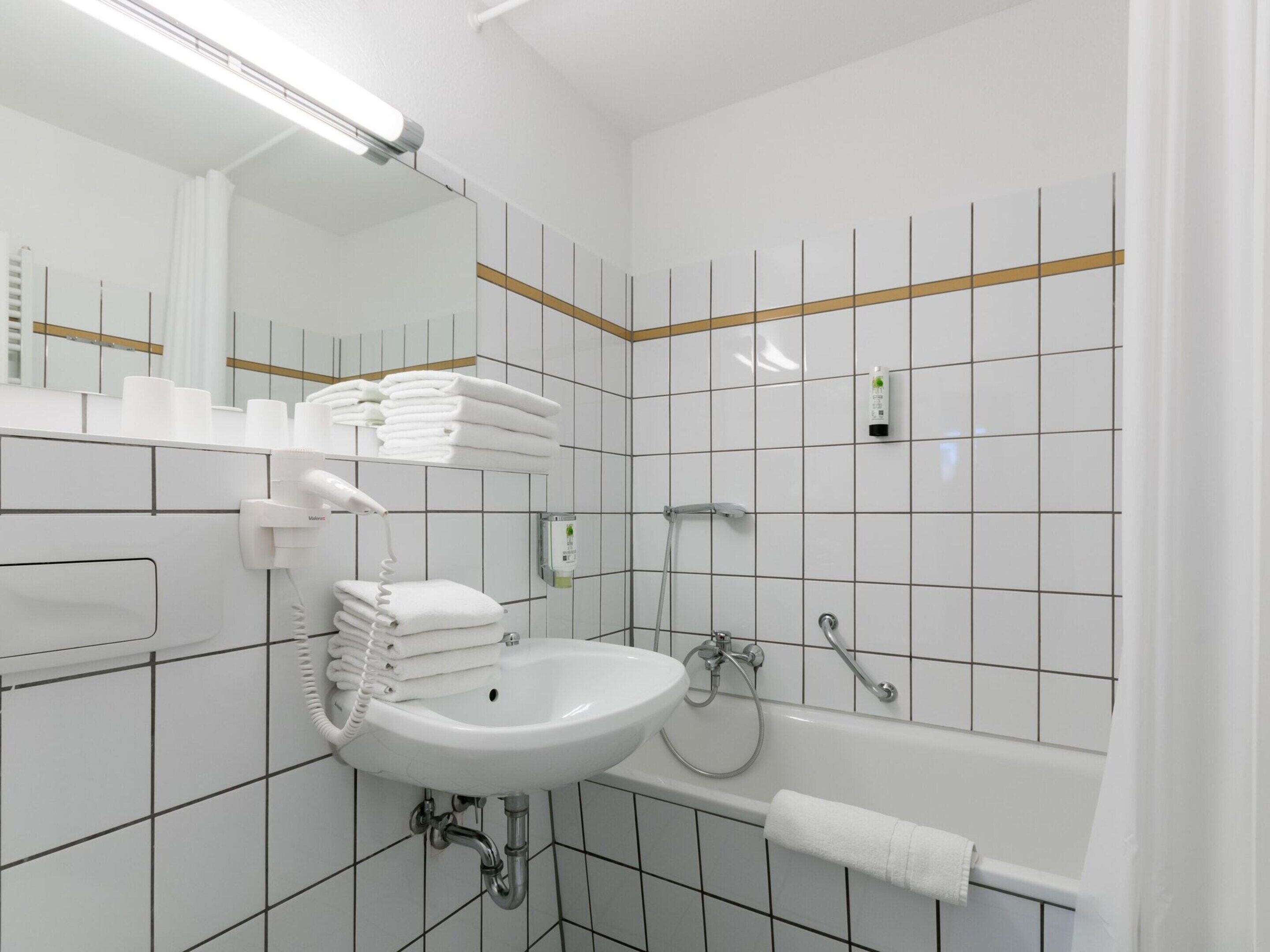 Un bagno moderno con lavandino bianco, uno specchio, un porta asciugamani e una vasca da bagno.