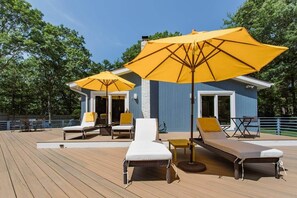 En solterrasse med liggestole og gule parasoller, et lille bord, og en blå bygning med en hvid dør.