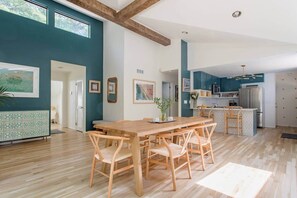 A spacious dining area with a wooden table and chairs, a kitchen with teal cabinets, and a large window providing natural light.