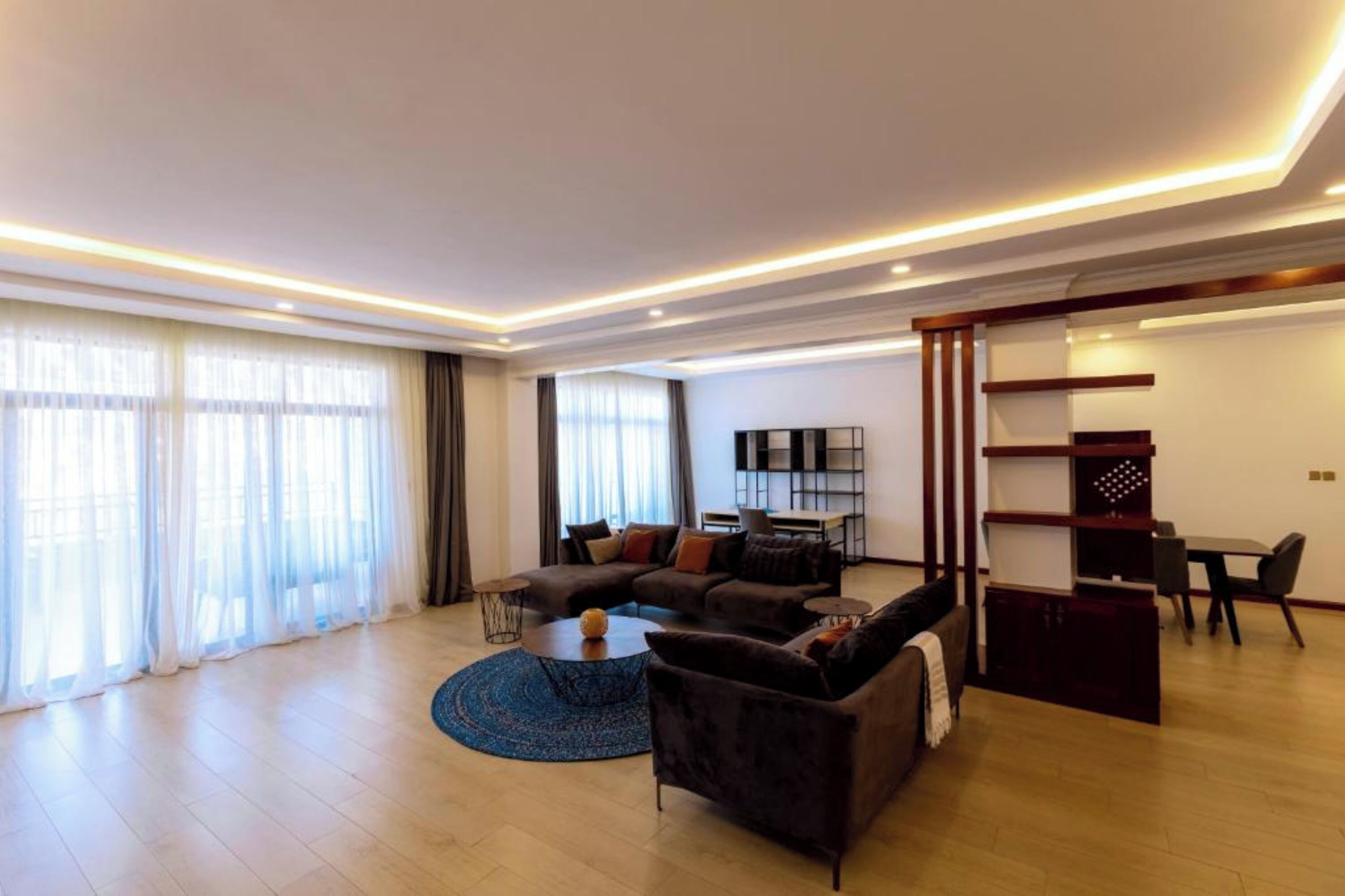 A modern living room with a sectional sofa, a coffee table, and a TV. There is a dining area with a table and chairs.