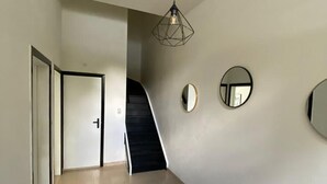 Un couloir avec un escalier, une porte et deux miroirs fixés au mur.