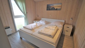 A bedroom with a large bed, two bedside tables, a window with curtains, and a painting on the wall. - Cottage in Granzow at 500 m From the Lake (Mirow)