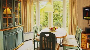 Ein Essbereich mit Erkerfenster, einem Tisch mit Stühlen, einer Obstschale und einem Schrank mit Glastüren.