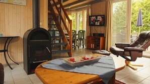Ein gemütliches Wohnzimmer mit Kamin, Fernseher, Essbereich und einer Treppe, die in eine obere Etage führt.