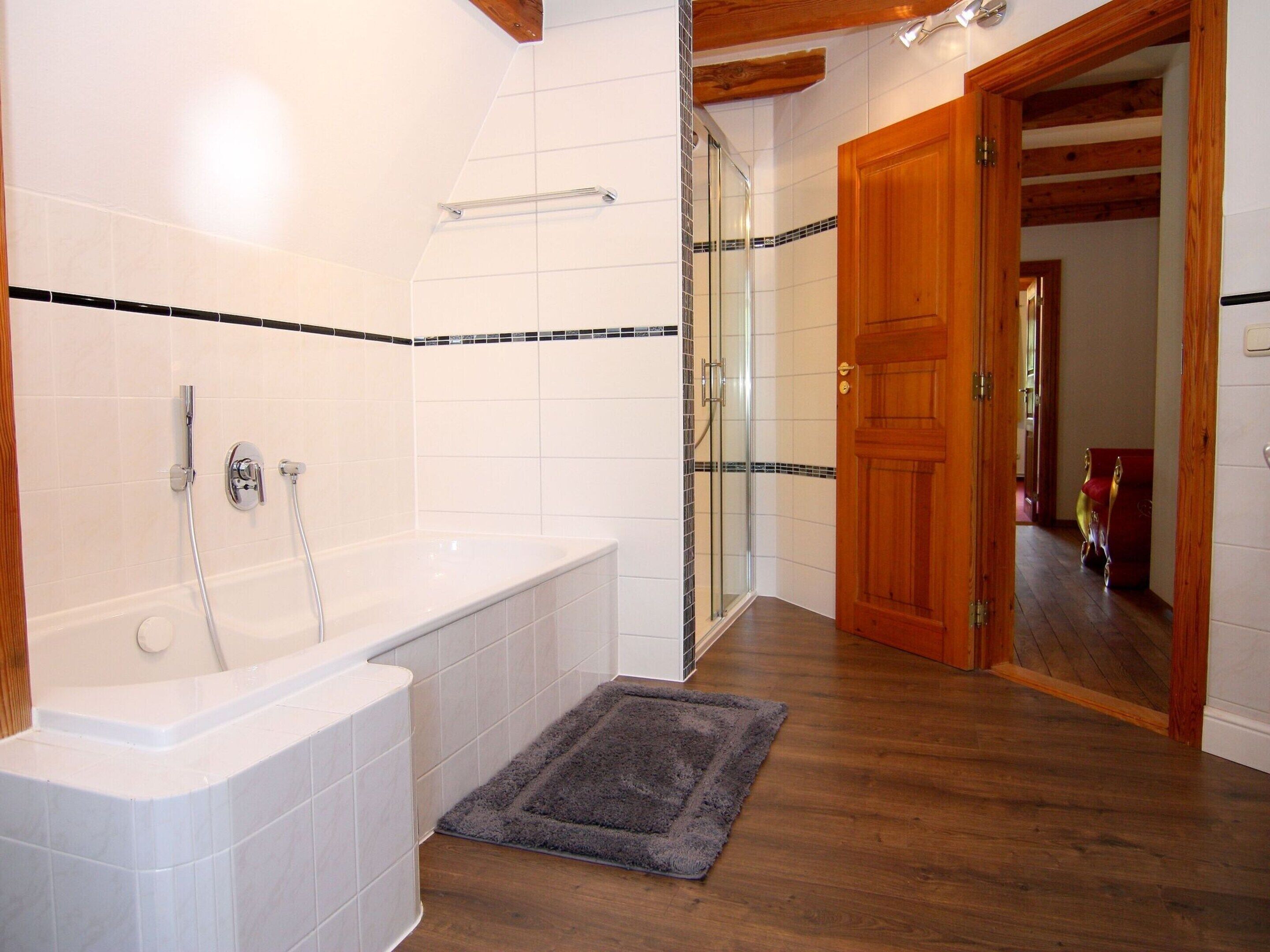 A bathroom with a bathtub, shower, and glass door leading to a hallway.