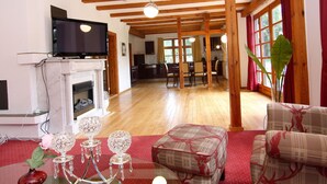 Ein geräumiges Wohnzimmer mit Kamin, Holzbalken, Fernseher und Essbereich.