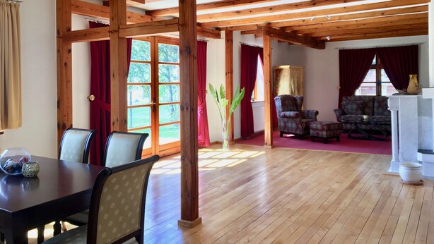 Ein geräumiger Raum mit Holzbalken, einem Essbereich mit Tisch und Stühlen sowie einer Sitzecke mit Sofas.
